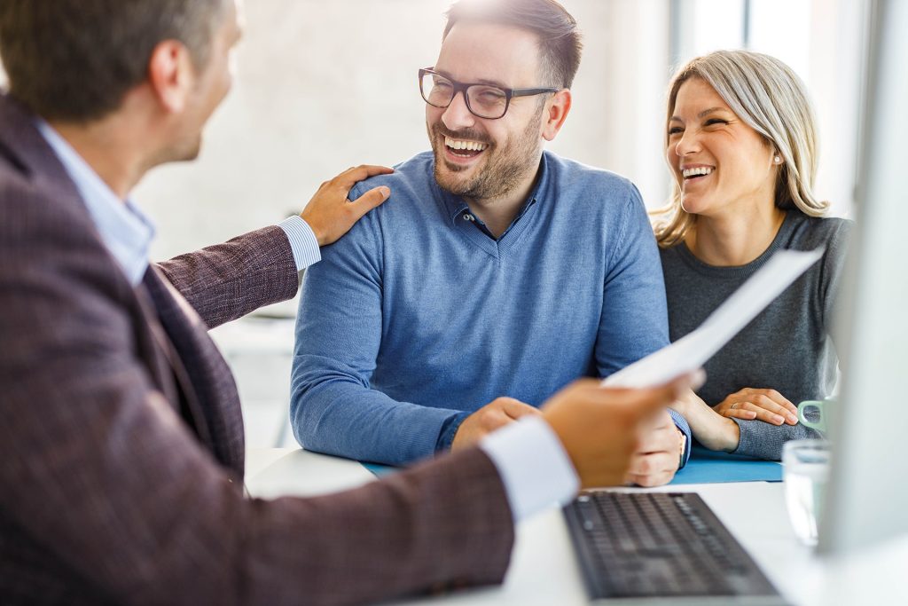 A couple meeting with a financial counselor in an office, smiling and reviewing paperwork.